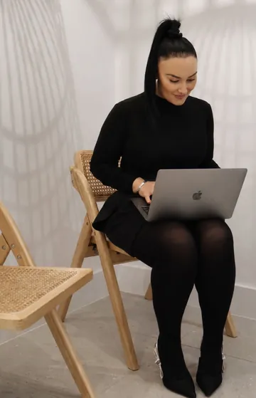 Chrystyl seated on a rattan chair, working on a laptop in a white clinic room